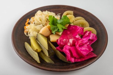 Kırsal bir tabakta çeşitli sebze turşusu yakın plan. Canlı pembe lahana, turşu ve taze otlar rengarenk ve iştah açıcı bir besin bileşimi oluşturur.