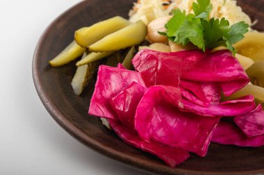 Kırsal bir tabakta çeşitli sebze turşusu yakın plan. Canlı pembe lahana, turşu ve taze otlar rengarenk ve iştah açıcı bir besin bileşimi oluşturur.