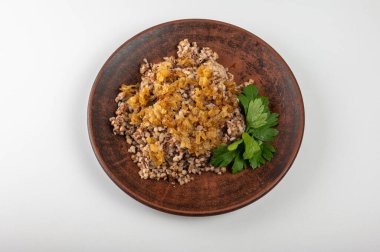 Geleneksel karabuğday lapası ve kırsal tabakta karamelize soğan. Sıcak, besleyici ve aromatik bir yemek, Doğu Avrupa mutfağında popüler, kilden bir tabakta, beyaz bir arka planda.