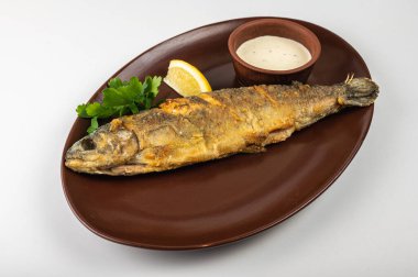 Kahverengi bir tabakta taze maydanoz, limon dilimi ve kremalı sosla servis edilen kızarmış balık. Lezzetli bir deniz ürünleri yemeği, restoran menüsü ya da yemek blogu için mükemmel.