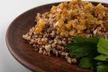 Geleneksel karabuğday lapası ve kırsal tabakta karamelize soğan. Sıcak, besleyici ve aromatik bir yemek, Doğu Avrupa mutfağında popüler, kilden bir tabakta, beyaz bir arka planda.