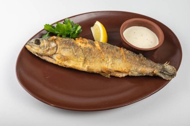 Hafif arka planda kızarmış balık, taze maydanozlu kahverengi bir tabak, bir dilim limon ve kremalı sos. Lokanta menüsü veya yemek blogu için uygun lezzetli bir deniz ürünleri yemeği.