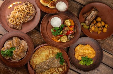 Geleneksel Doğu Avrupa mutfağı kırsal kil tabaklarda servis edilir. Ahşap bir arka planda et, patates, krep, hamur tatlısı ve ızgara sebze gibi ev yapımı yemekler var.