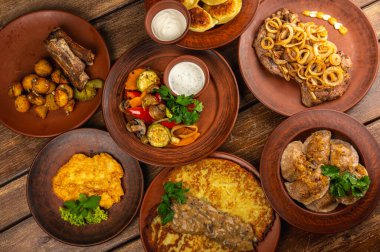 Geleneksel Doğu Avrupa mutfağı kırsal kil tabaklarda servis edilir. Ahşap bir arka planda et, patates, krep, hamur tatlısı ve ızgara sebze gibi ev yapımı yemekler var.