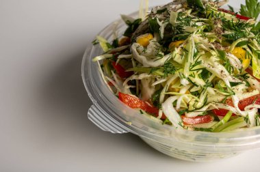 Doldurulmuş biberli taze lahana salatası, mısır, yeşil soğan ve plastik bir kabın içinde dereotu. Sağlıklı vejetaryen yiyecekler, canlı ve besleyici yemekler. Temiz beyaz arkaplan