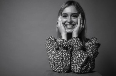 Siyah beyaz fotoğraf, portre, çiçekli bir elbise içindeki düşünceli, duygusal genç kız yüzüne yakın düşünceli eller, arka planda düşünceler. Yüz ifadesi, modern moda ve kendine güvenen konum, duygular, jestler.