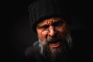 Siyah bereli kızgın sakallı adam ve kameraya homurdanan gözlükler. Gösterişsiz ışıklandırma dramatik portre, anlamlı yüz, duygusal gerilim, karanlık arka plan