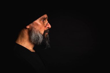 Portre, keskin bakışlı, somurtkan suratlı, gözlüklü, örgü şapkalı ve yana bakan olgun bir adam. Karanlık arka planda güçlü duygularla dizginlenmiş dramatik bir portre..