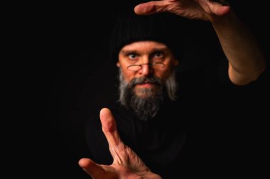 Kameraya uzanan sakallı ve gözlüklü gergin bir adamın dramatik portresi. Alçak tuş aydınlatma, duygusal ifade, karanlık arkaplan, gizem kavramı