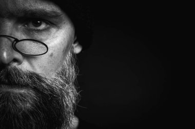 Siyah örgü şapkalı, sakallı ve gözlüklü kendine güvenen olgun bir adamın siyah beyaz portresi. Keskin bir bakış, duygusal gri bir sakal ve siyah bir yelek. Koyu bir arkaplanda zarif bir portre..