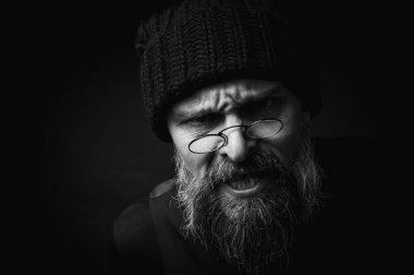 Siyah örgü şapkalı, sakallı ve gözlüklü kendine güvenen olgun bir adamın siyah beyaz portresi. Keskin bir bakış, duygusal gri bir sakal ve siyah bir yelek. Koyu bir arkaplanda zarif bir portre..