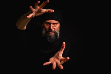 Kameraya uzanan sakallı ve gözlüklü gergin bir adamın dramatik portresi. Alçak tuş aydınlatma, duygusal ifade, karanlık arkaplan, gizem kavramı