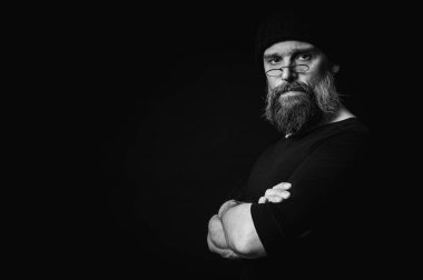 Siyah örgü şapkalı, sakallı ve gözlüklü kendine güvenen olgun bir adamın siyah beyaz portresi. Keskin bir bakış, duygusal gri bir sakal ve siyah bir yelek. Koyu bir arkaplanda zarif bir portre..