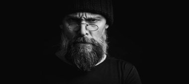 Siyah örgü şapkalı, sakallı ve gözlüklü kendine güvenen olgun bir adamın siyah beyaz portresi. Keskin bir bakış, duygusal gri bir sakal ve siyah bir yelek. Koyu bir arkaplanda zarif bir portre..