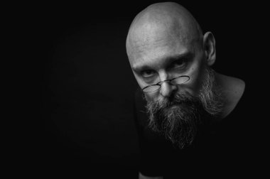 Kısa, kel ve gözlüklü, kendine güvenen olgun bir adamın siyah beyaz portresi. Keskin bir bakış, gri bir sakal ve siyah bir yelek. Koyu bir arka planda zarif, kısıtlı bir portre..