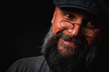 Gri pirinç muştalı, gri kazaklı ve siyah arka planda kameraya bakan duygusal sakallı bir adamın portresi. Bastırılmış aydınlatma, anlamlı yüz, duygusal gerilim, karanlık arka plan dramatik portre.