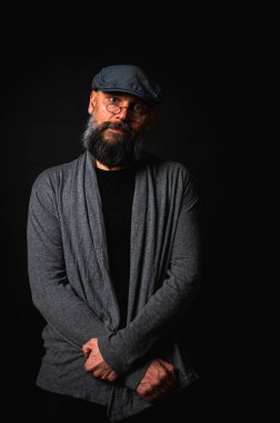 Gri pirinç muştalı, gri kazaklı ve siyah arka planda kameraya bakan duygusal sakallı bir adamın portresi. Bastırılmış aydınlatma, anlamlı yüz, duygusal gerilim, karanlık arka plan dramatik portre.