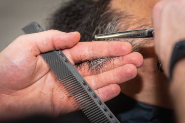 Modern bir berber dükkanında elektrikli makasla sakal kesen bir berberin yakın çekimi. Profesyonel erkek bakımı ve sakal bakımı, seçici odaklanma