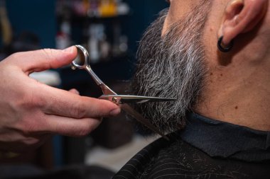 Modern bir berber dükkanında elektrikli makasla sakal kesen bir berberin yakın çekimi. Profesyonel erkek bakımı ve sakal bakımı, seçici odaklanma