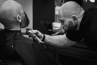 Siyah beyaz fotoğraf, modern bir berber dükkanında sakalı elektrikli makasla buduyor. Profesyonel erkek bakımı ve sakal bakımı, seçici odaklanma