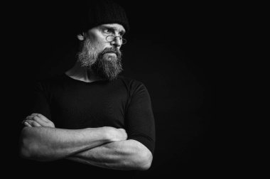 Siyah beyaz, kendine güvenen, kollarını önünde kavuşturmuş, örgü şapka ve gözlük takan olgun bir adamın şık portresi. Bakışları, gri sakalı ve siyah yeleği vardı. Koyu arkaplanda zarif bir portre