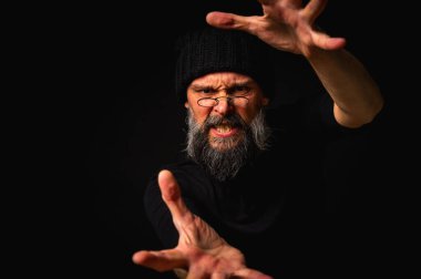 Kameraya uzanan sakallı ve gözlüklü enerjik bir adamın dramatik portresi. Elleriyle çekmeye çalışıyor. İnce ışıklandırma, duygusal ifade, karanlık arkaplan, gizemli konsept