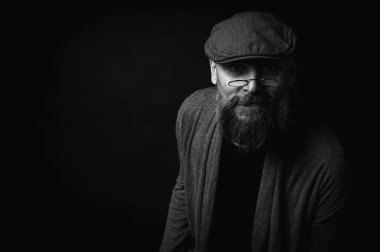 Siyah ve beyaz, siyah arka planda gözlüklü ve şapkalı ciddi sakallı bir adamın Macro portresi. Şık, kendine güvenen ve gizemli bir ifadeyle etkileyici bir bakış.