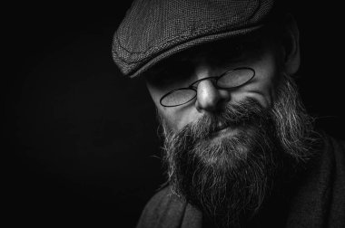 Siyah ve beyaz, siyah arka planda gözlüklü ve şapkalı ciddi sakallı bir adamın Macro portresi. Şık, kendine güvenen ve gizemli bir ifadeyle etkileyici bir bakış.