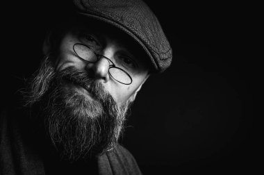 Siyah ve beyaz, siyah arka planda gözlüklü ve şapkalı ciddi sakallı bir adamın Macro portresi. Şık, kendine güvenen ve gizemli bir ifadeyle etkileyici bir bakış.