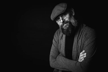 Siyah ve beyaz, siyah arka planda gözlüklü ve şapkalı ciddi sakallı bir adamın Macro portresi. Şık, kendine güvenen ve gizemli bir ifadeyle etkileyici bir bakış.