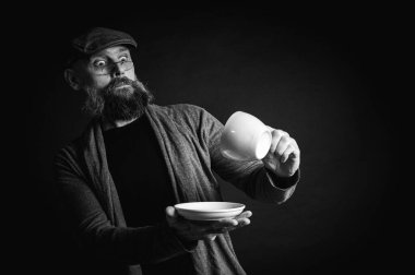 Siyah ve beyaz portre, şık şapkalı ve gözlüklü olgun sakallı bir adam gizemli bir gülümsemeyle bir fincan kahve sunuyor. Olağanüstü aydınlatma ve karanlık arka plan eski moda bir hava yaratıyor..