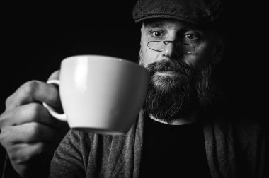 Siyah ve beyaz portre, şık şapkalı ve gözlüklü olgun sakallı bir adam gizemli bir gülümsemeyle bir fincan kahve sunuyor. Olağanüstü aydınlatma ve karanlık arka plan eski moda bir hava yaratıyor..