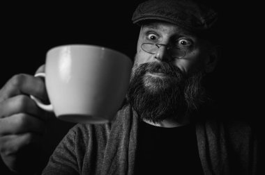 Siyah ve beyaz portre, şık şapkalı ve gözlüklü olgun sakallı bir adam gizemli bir gülümsemeyle bir fincan kahve sunuyor. Olağanüstü aydınlatma ve karanlık arka plan eski moda bir hava yaratıyor..