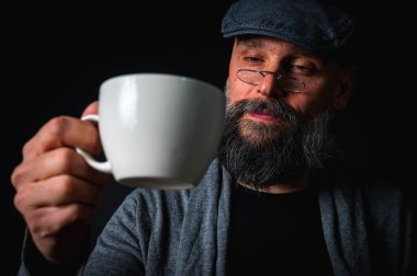 Şık şapkalı ve gözlüklü olgun sakallı bir adam gizemli bir gülümsemeyle bir fincan kahve sunuyor. Dramatik ışıklandırma ve karanlık arkaplan klasik mod yaratır