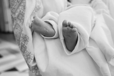 Geleneksel Hıristiyan vaftiz töreni sırasında beyaz giysili bebek ayaklarının yakın çekimi. Yumuşak ışık ve kutsal atmosfer