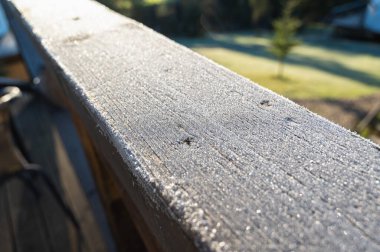 Güneş ışığı ve yumuşak arka plan bulanıklığı ile sabah çiğ ile kaplı ahşap korkuluklara yakın çekim. Doğa, doku, tazelik ve odaklanma temaları için mükemmel bir görüntü.