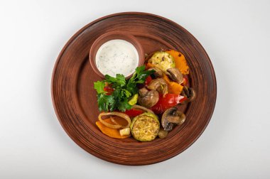 Kremalı soslu, kahverengi bir tabakta nefis kızarmış sebzeler. Sağlıklı bir yemek için ızgara kabak, mantar, dolmalık biber, soğan ve maydanoz garnitürü.