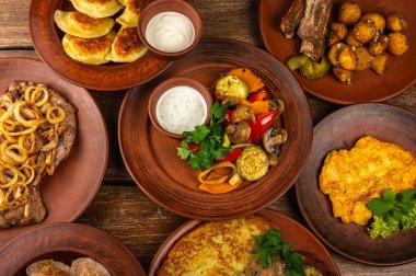 Geleneksel Doğu Avrupa mutfağı kırsal kil tabaklarda servis edilir. Ahşap bir arka planda et, patates, krep, hamur tatlısı ve ızgara sebze gibi ev yapımı yemekler var.