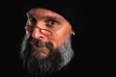 duygusal, yüz, siyah şapkalı ve kameraya bakan sakallı bir adamın kızgın portresi. Bastırılmış aydınlatma, anlamlı yüz, duygusal gerilim, karanlık arka plan dramatik portre