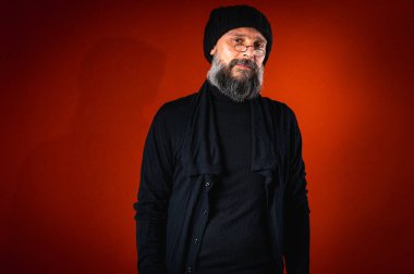 Sakallı, gözlüklü, siyah şapkalı, parlak turuncu arka planda duran şık ve olgun bir adamın portresi. Moda, kendine güven, modern görünüş.