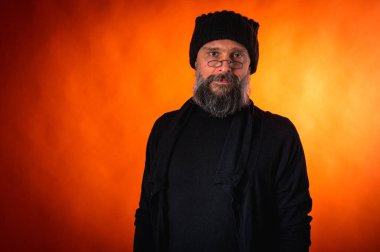 Sakallı, gözlüklü, siyah şapkalı, parlak turuncu arka planda duran şık ve olgun bir adamın portresi. Moda, kendine güven, modern görünüş.