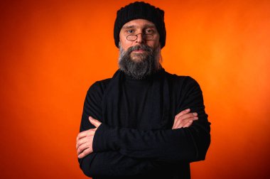 Kollarını önünde kavuşturmuş, turuncu arka planda kep ve gözlük takan kendinden emin olgun bir adamın portresi. Keskin bir bakış, gri bir sakal ve siyah bir yelek. Şık, ihtiyatlı bir portre, bir yazı için alan.