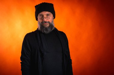 Sakallı, gözlüklü, siyah şapkalı, parlak turuncu arka planda duran şık ve olgun bir adamın portresi. Moda, kendine güven, modern görünüş.