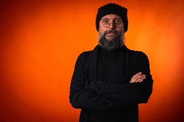 Kollarını önünde kavuşturmuş, turuncu arka planda kep ve gözlük takan kendinden emin olgun bir adamın portresi. Keskin bir bakış, gri bir sakal ve siyah bir yelek. Şık, ihtiyatlı bir portre, bir yazı için alan.