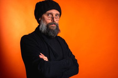 Kollarını önünde kavuşturmuş, turuncu arka planda kep ve gözlük takan kendinden emin olgun bir adamın portresi. Keskin bir bakış, gri bir sakal ve siyah bir yelek. Şık, ihtiyatlı bir portre, bir yazı için alan.