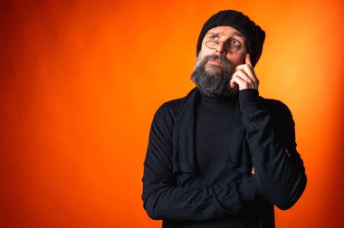 Siyah şapkalı, sakallı ve gözlüklü, parlak turuncu arka planda duran zarif olgun bir adamın portresi. Moda, kendine güven, modern görünüş.
