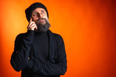 Siyah şapkalı, sakallı ve gözlüklü, parlak turuncu arka planda duran zarif olgun bir adamın portresi. Moda, kendine güven, modern görünüş.