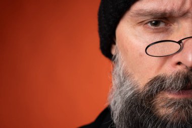 Sakallı, gözlüklü, siyah şapkalı, parlak turuncu arka planda duran şık ve olgun bir adamın portresi. Moda, kendine güven, modern görünüş.