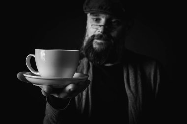 Siyah beyaz portre, siyah şapkalı ve gözlüklü duygusal sakallı adam, kameraya düşünceli bir bakış. Bastırılmış aydınlatma, anlamlı yüz, duygusal gerilim, karanlık arka plan dramatik portre.