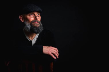 Gözlüklü ve sakallı, etkileyici ışıklandırmayla stüdyoda poz veren düşünceli olgun bir adam. Bilgeliğin kavramsal portresi, özgüven ve siyah arkaplan üzerine iç gözlem